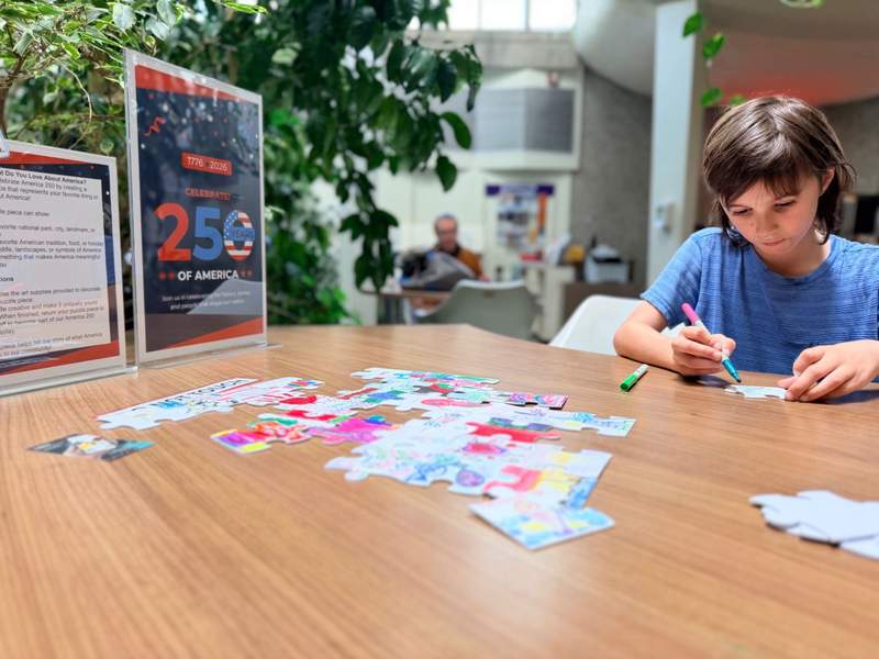 Boy coloring a puzzle piece at table with other puzzle pieces in front.