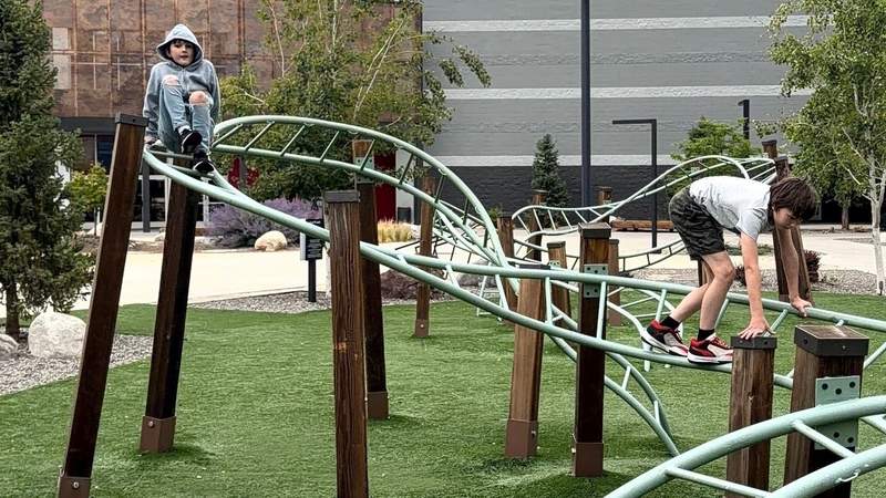 Two boys climb an outdoor ladder climbing structure.