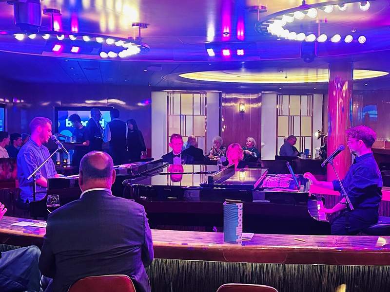 Alt text: Musicians performing at a dueling piano lounge onboard a Holland America cruise ship