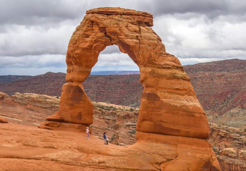 Horizontal view of Delicate Arch standing on a natural red rock plateau in Arches National Park Utah
