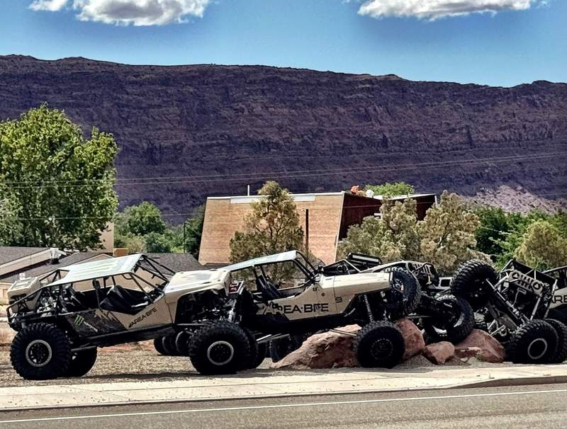 Custom off-road rock crawlers branded parked on rocks in front of red rock cliffs in Moab, Utah.