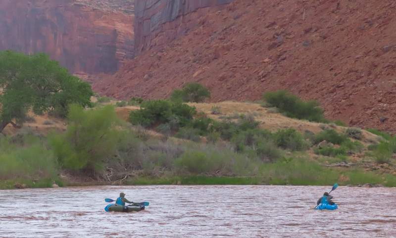 Horizontal shot of kayakers on a calm stretch of the Colorado River with high canyon walls in the background