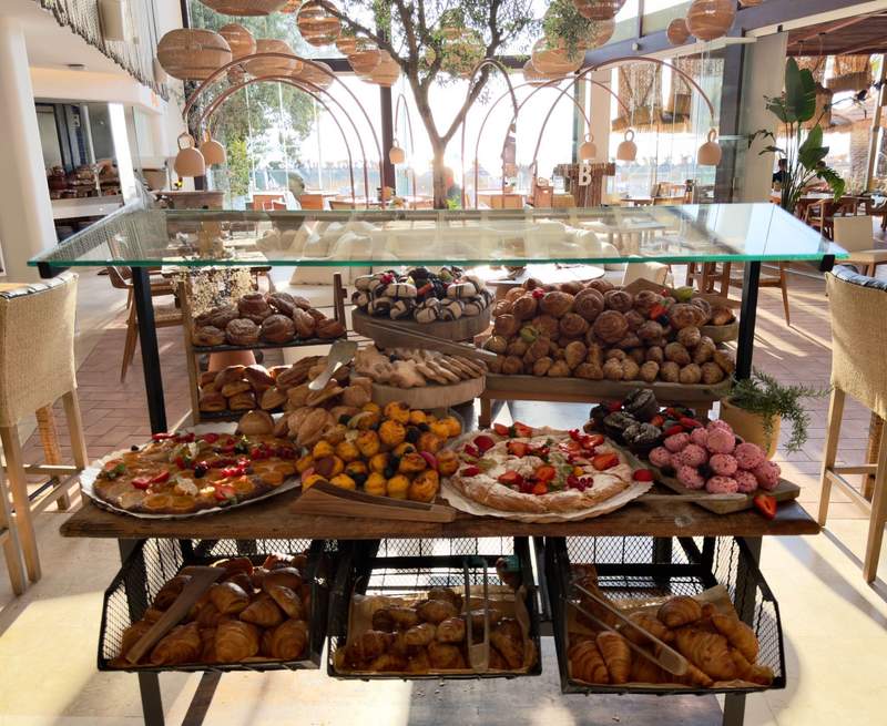 Tiered breakfast display filled with croissants, pink frosted pastries, cakes and other baked sweets