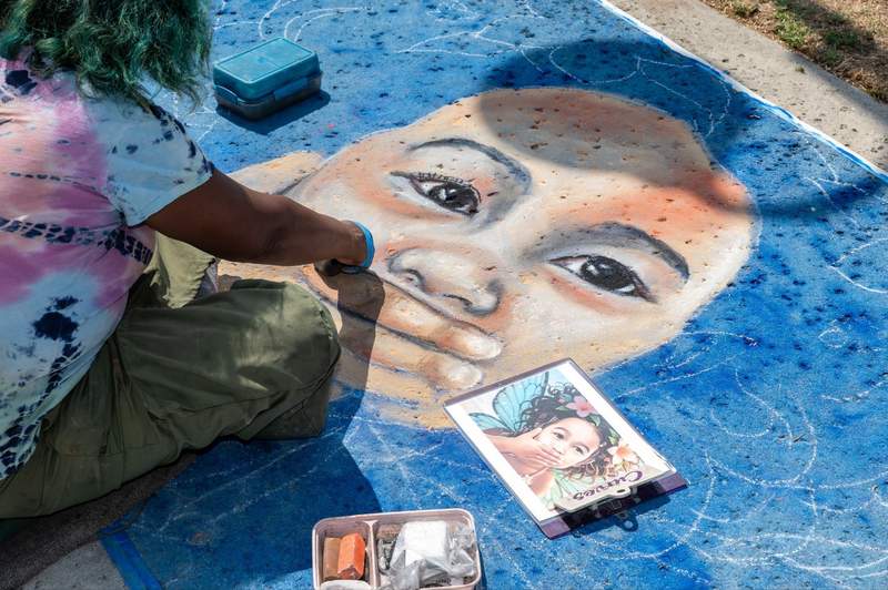 artist kneeling on pavement painting a large chalk portrait of a childs face
