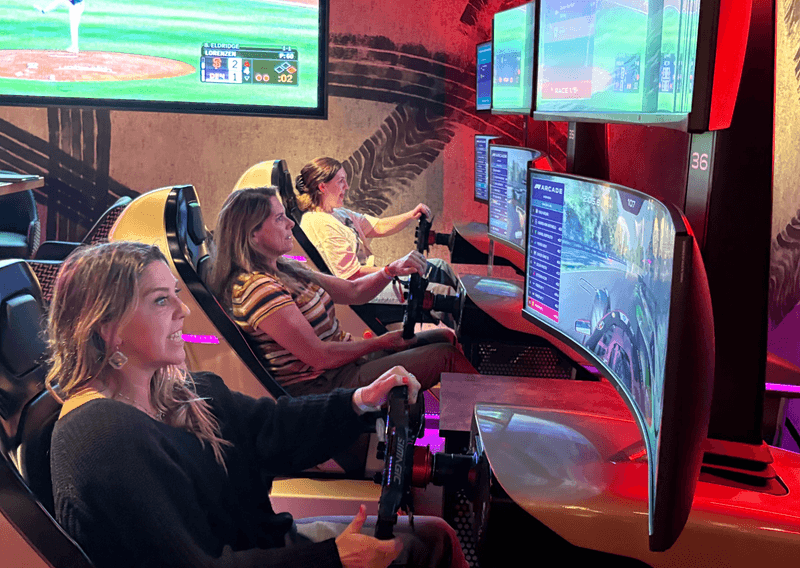 People racing on simulator machines with steering wheels at an arcade
