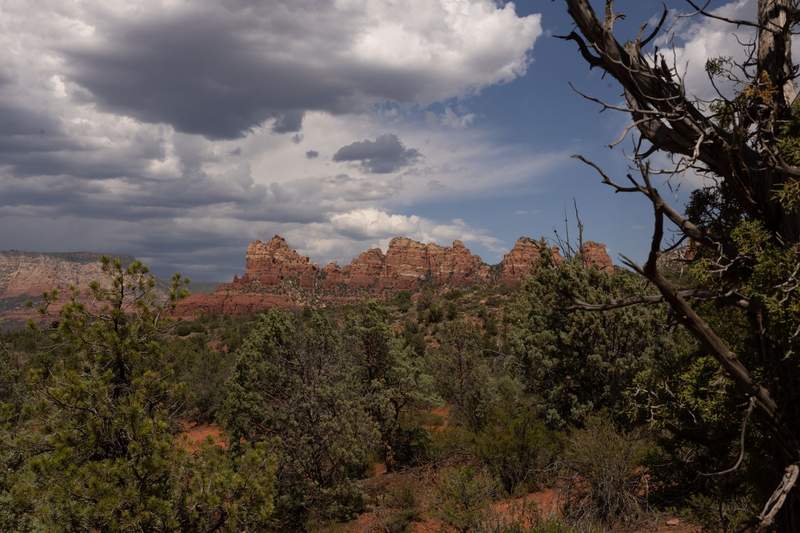 Sedona red-rock formations rise above a juniper-covered landscape beneath dramatic monsoon clouds.