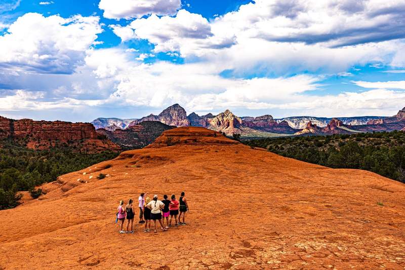 A group of Jeepsters stands on a broad red-rock overlook with Sedona’s colorful cliffs and mesas stretching across the horizon.