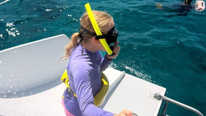 Girl wearing a snorkel mask and life vest preparing to enter the turquoise water from a boat in the Turks and Caicos.