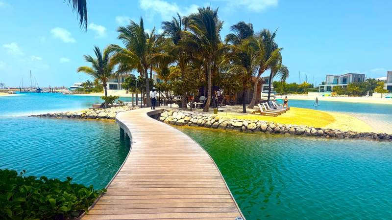 Wooden boardwalk leading to a palm-covered private island surrounded by turquoise lagoon water at South Bank Resort in the Turks and Caicos.