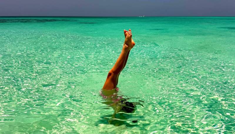 Girl doing an underwater handstand in shallow, crystal-clear turquoise water in the Turks and Caicos.