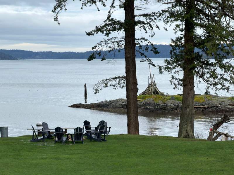 Adirondack chairs surround a fire pit on a grassy lawn overlooking the calm waterfront and rocky shoreline at Pebble Cove Farm on Orcas Island.