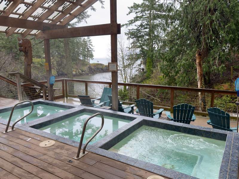 Three outdoor soaking pools sit on a wooden deck surrounded by evergreen forest, overlooking a quiet cove at Doe Bay Resort on Orcas Island.