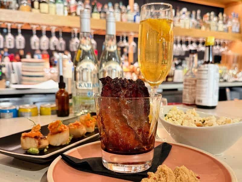 Seared scallops, a dark cocktail topped with crisp bacon, sparkling wine and popcorn create a playful spread at the bar.