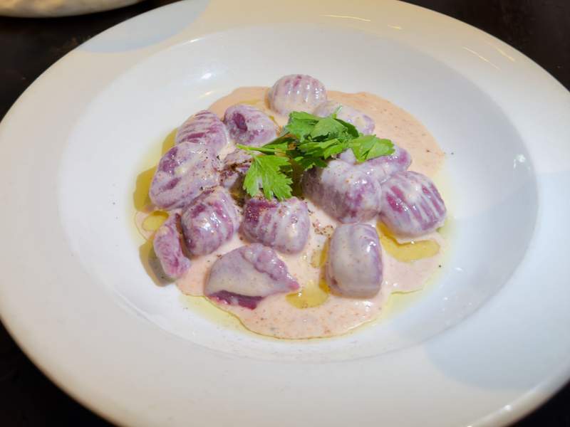 Purple gnocchi are coated in a pale creamy sauce with olive oil, black pepper and bright green parsley.