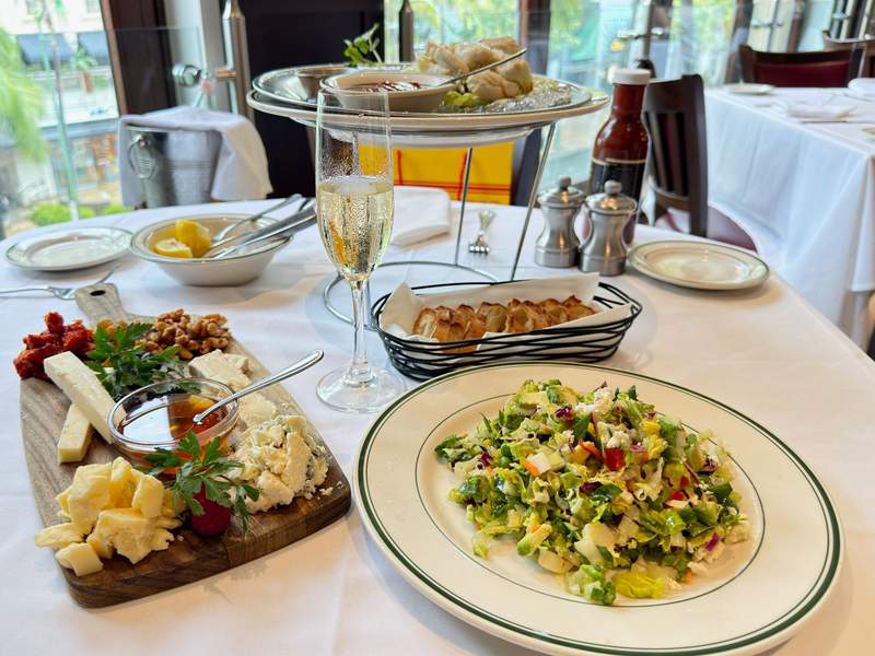 A colorful Wolfgang’s Steakhouse lunch spread with creamy and blue cheeses, walnuts, dried fruit, a crisp chopped salad, toasted bread and a chilled glass of sparkling wine.
