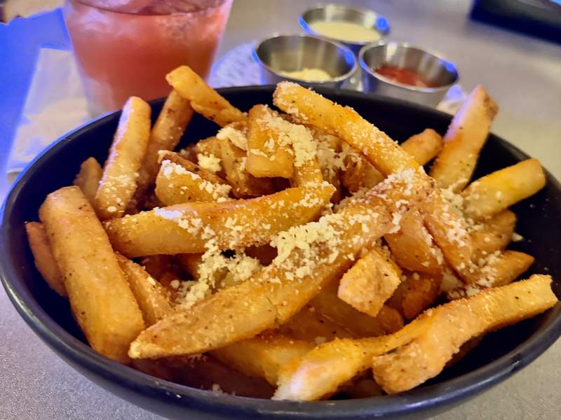 A heaping bowl of crisp golden fries is dusted with grated cheese and served with three dipping sauces at RumFire.