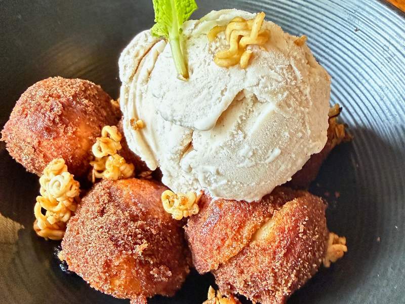 Cinnamon-brown malasada bites surround a large scoop of pale horchata ice cream, with caramel corn scattered around the plate.