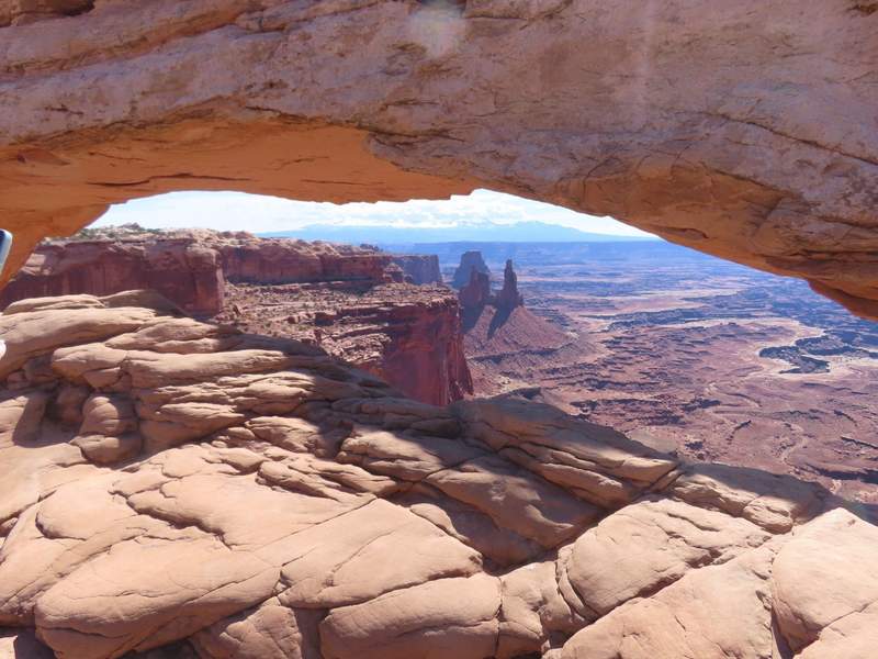 Panoramic view of deep red rock canyons and sandstone rock formations framed underneath natural stone Mesa Arch in Canyonland National Park.