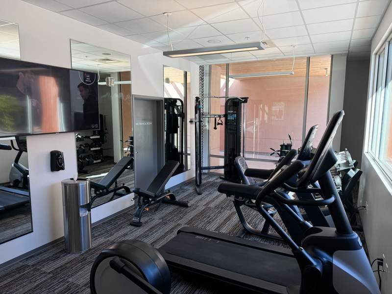 Modern hotel gym with treadmills recumbent bikes weight benches and wall mirrors facing large windows.