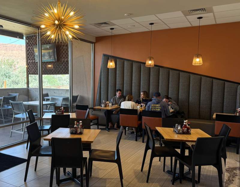 Guests eating breakfast inside a brightly lit modern cafe with wooden tables geometric wall padding and starburst light fixtures.