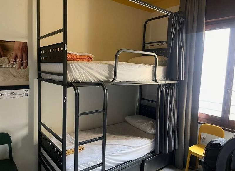 Black metal bunk beds with privacy curtains, white bedding and a ladder inside a shared dorm room at Ostello Bello in Milan, Italy.