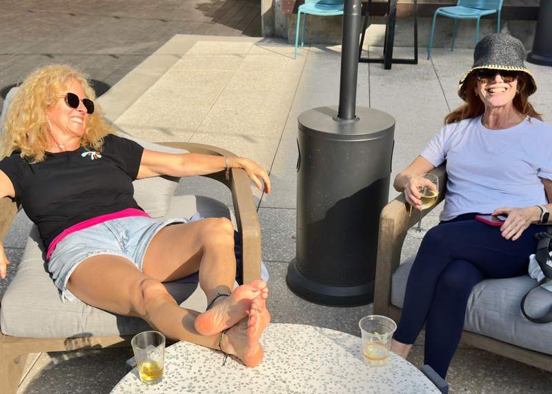 Two women lounging and sipping wine in cushiony patio chairs