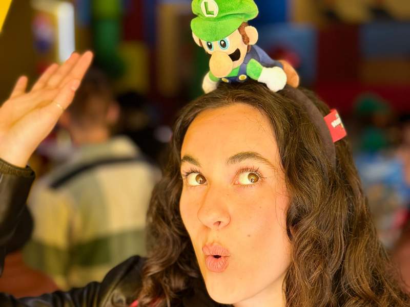 Stuffed Mario toy accented in green on top of the head of a young woman