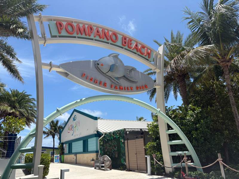 Entrance sign for Pompano Beach Fisher Family Pier surrounded by palm trees