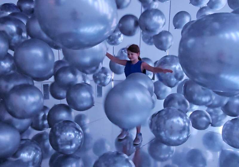 A young girl surrounded by silver balloons in an interactive balloon museum. 