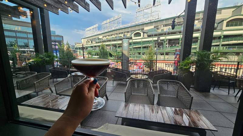 A woman holding up an espresso martini in front of Wrigley Stadium.  