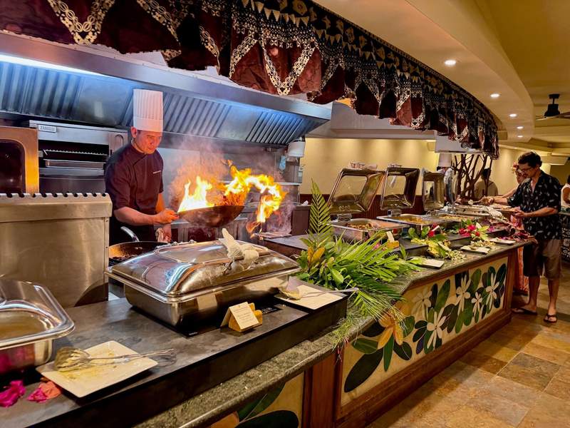 Chef in kitchen tossing flaming food in a wok.