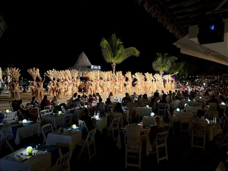 Large group of dancers in Polynesian costumes dancing on front of diners