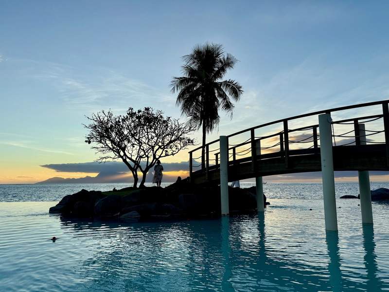 A lone woman seems to contemplate existence on a small island connected to the resort via a walking bridge.