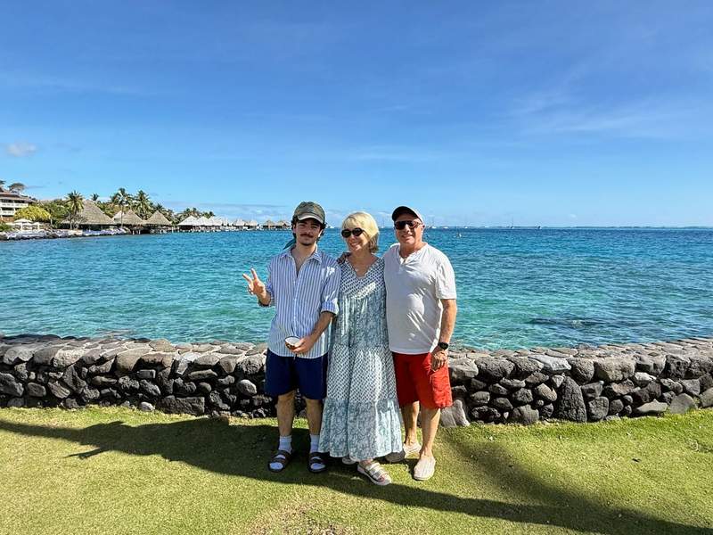 Author and family pose by a small rock wall overlooking the ocean with overwater bungalows in the background.