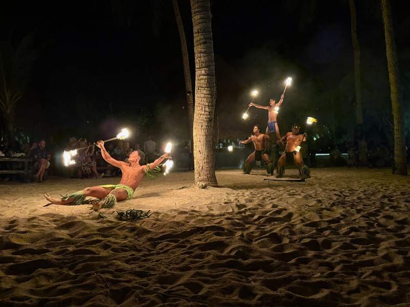 Several men fire dancing for a crowd on a beach.