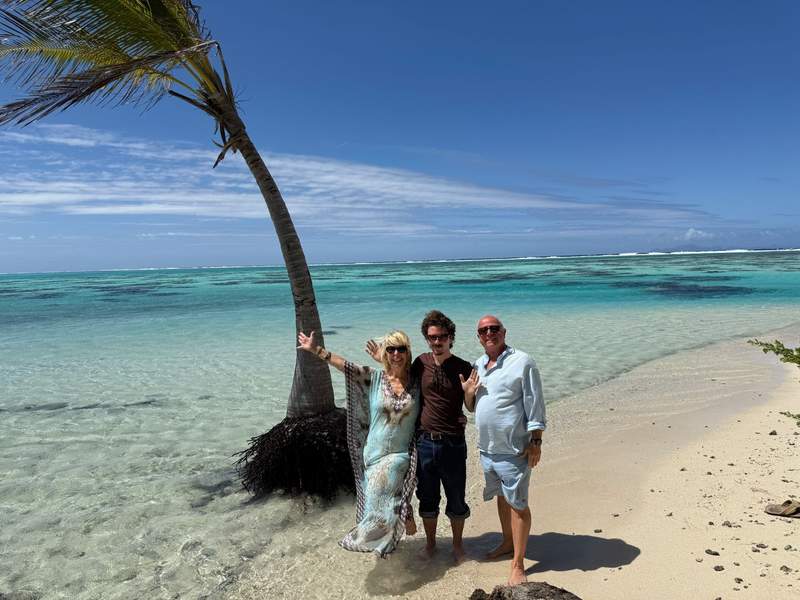 Author and family posing next to a lone palm tree on a beach with turquoise blue water.