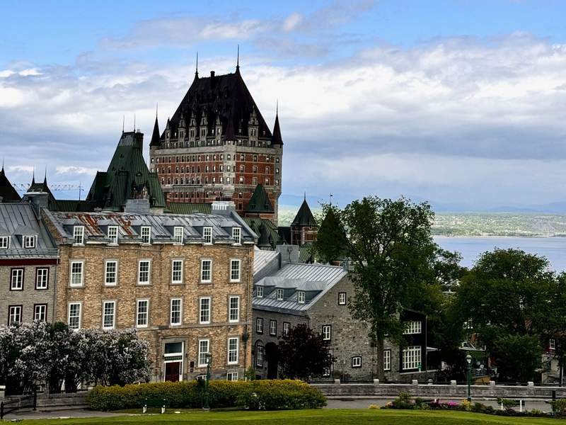 Red brick castle hotel with pointed black roof and steeples touching the sky overlooking the Saint Lawrence River.