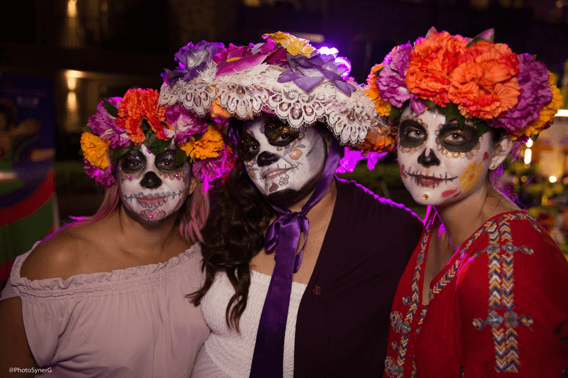 Three women wearing colorful Catrina face paint and flower crowns during Dia de los Muertos celebrations.