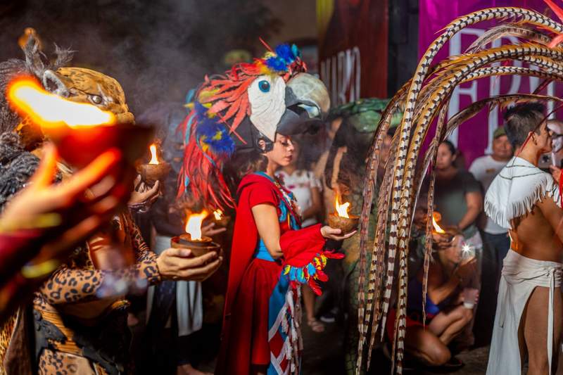 Performers in colorful Maya-inspired costumes carry ceremonial flames during a cultural celebration at Sandos Caracol in Mexico.