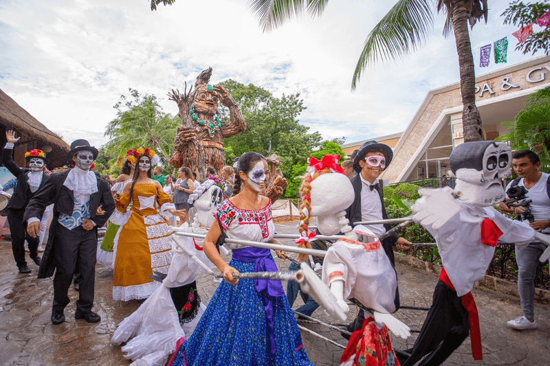 Catrina performers and skeleton puppets parade through Sandos Caracol during Dia de los Muertos celebrations in Mexico.