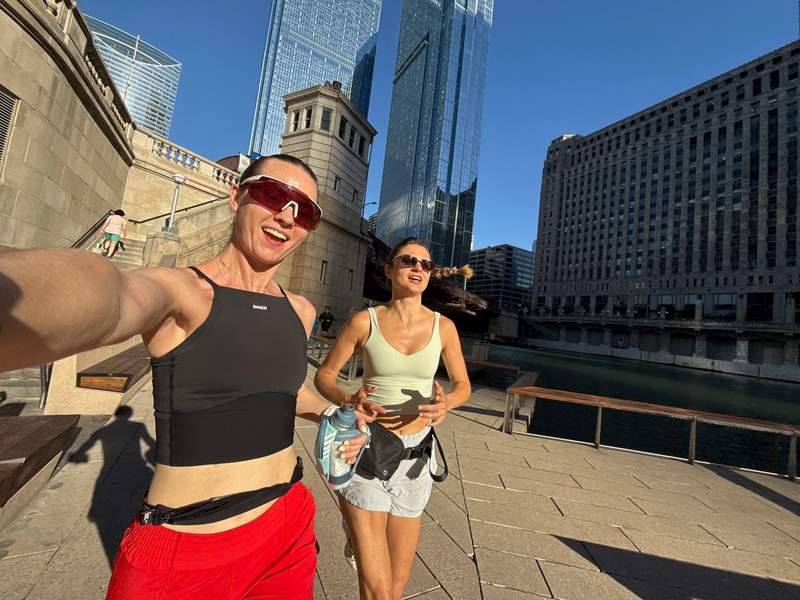 Selfie of two women jogging on Chicago Riverwalk sunny day with river stone bridge tower and downtown skyscrapers in background