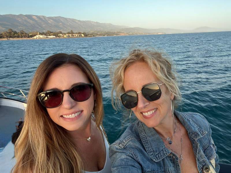 Two smiling women on a boat with views of the ocean, Santa Barbara coastline and mountains in the background