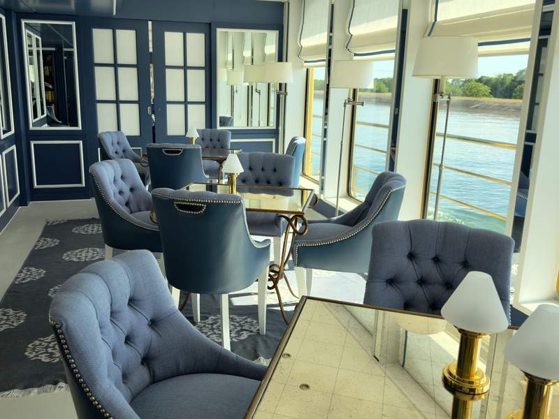 Sitting area with blue tufted chairs, tables and lamps overlooking the river.