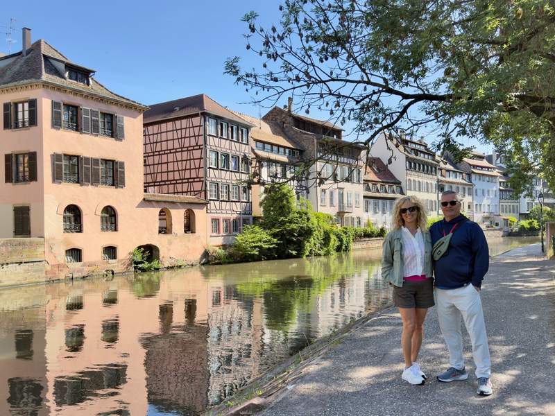 A couple posing next to Alsatian architecture reflected in the Ill River.