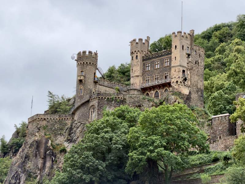 Giant brown rock castle built into a cliff and surrounded by green trees.