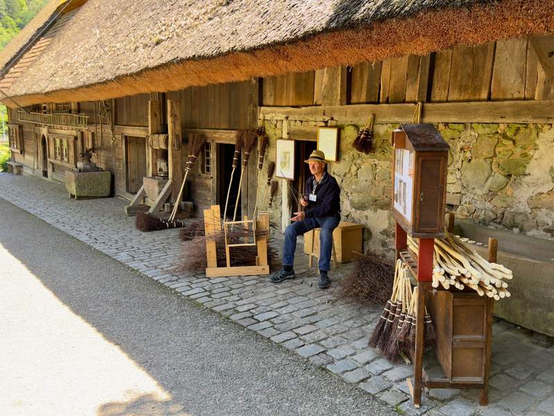 Broom maker in front of a replica of a barn demonstrates how a broom was made in the Black Forest.
