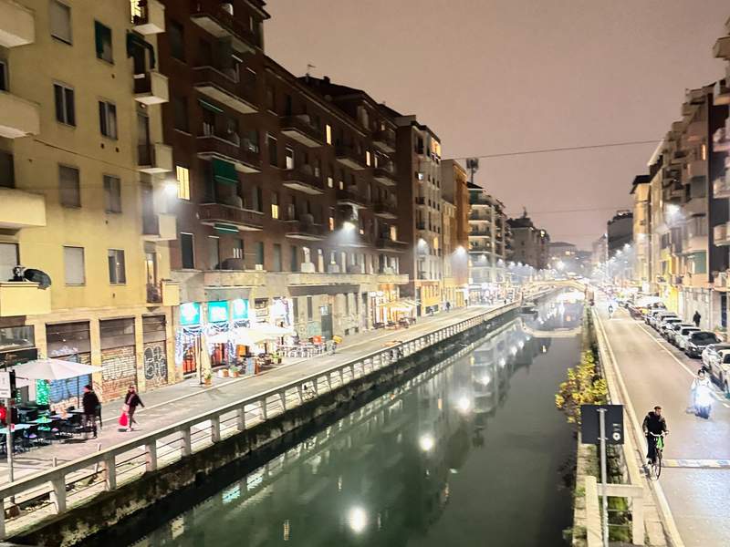 Buildings on both sides of a greenish colored canal and people on bikes and scootersin the Navigli district of Milan