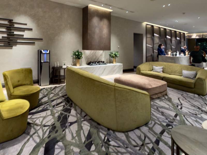 Hilton Milan lobby with curved green sofas and chairs, a large upholstered ottoman, patterned carpet and the reception desk in the background.