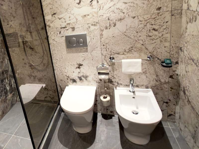 Hilton Milan guest bathroom finished in patterned marble with a glass-enclosed shower, toilet and separate bidet.