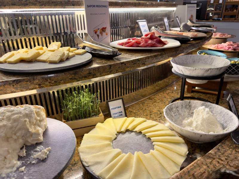 Hilton Milan breakfast buffet with platters of sliced Italian cheeses, soft cheese and cured meats displayed on a stone counter.